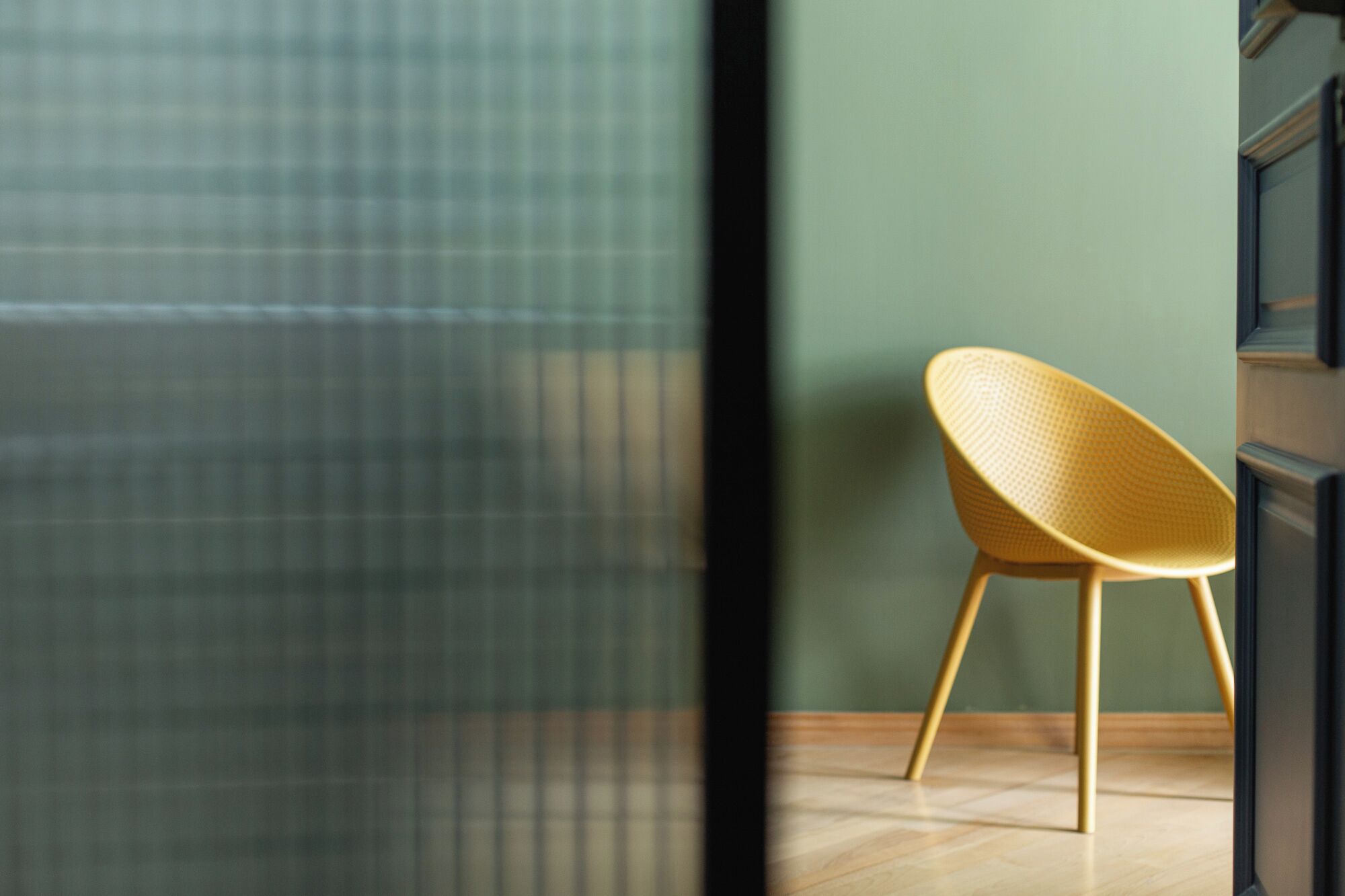 Una habitación con piso de madera, una silla trenzada amarilla y una pared verde.