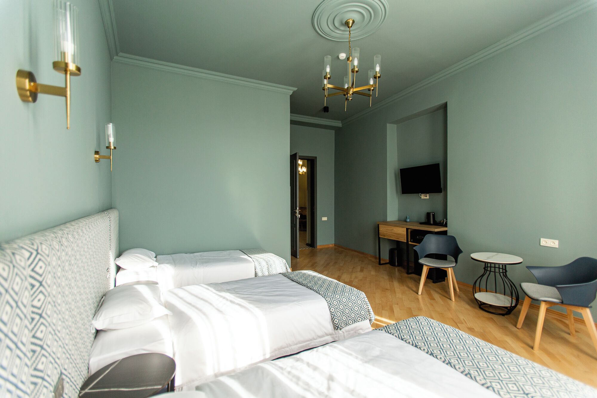 Une chambre d’hôtel avec un grand lit, un bureau, une chaise, une télévision et un lustre.