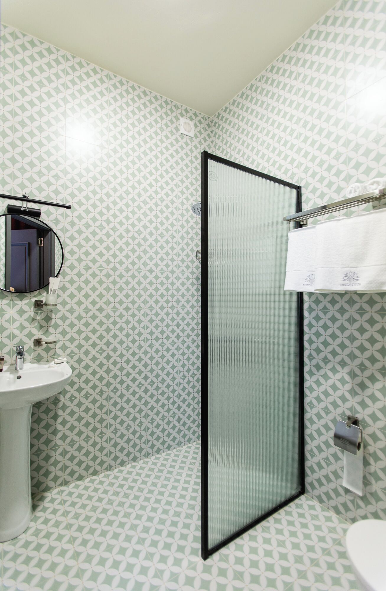 A bathroom with a white sink, a mirror, a towel rack, and a shower area with a glass door.