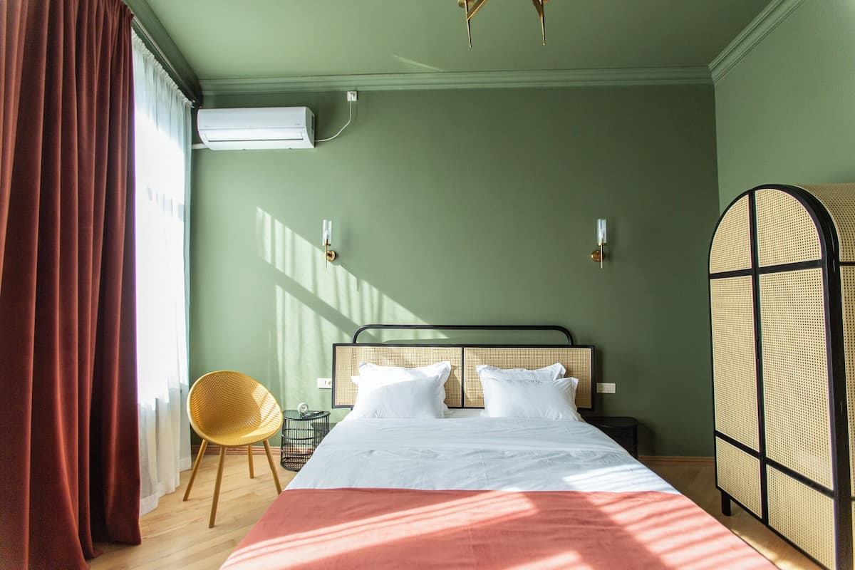A room with a bed, a chair, a wall-mounted air conditioner, and a partition with a woven design.