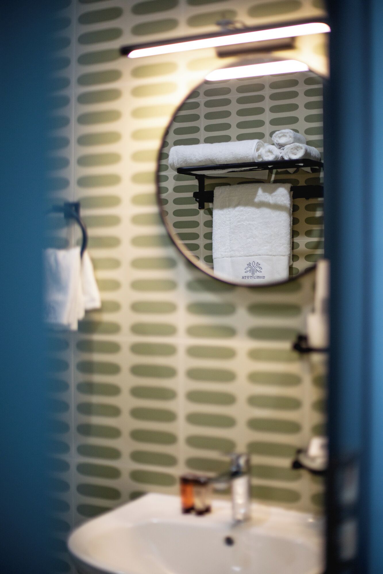 A bathroom with a round mirror, a sink, and a towel rack with towels.