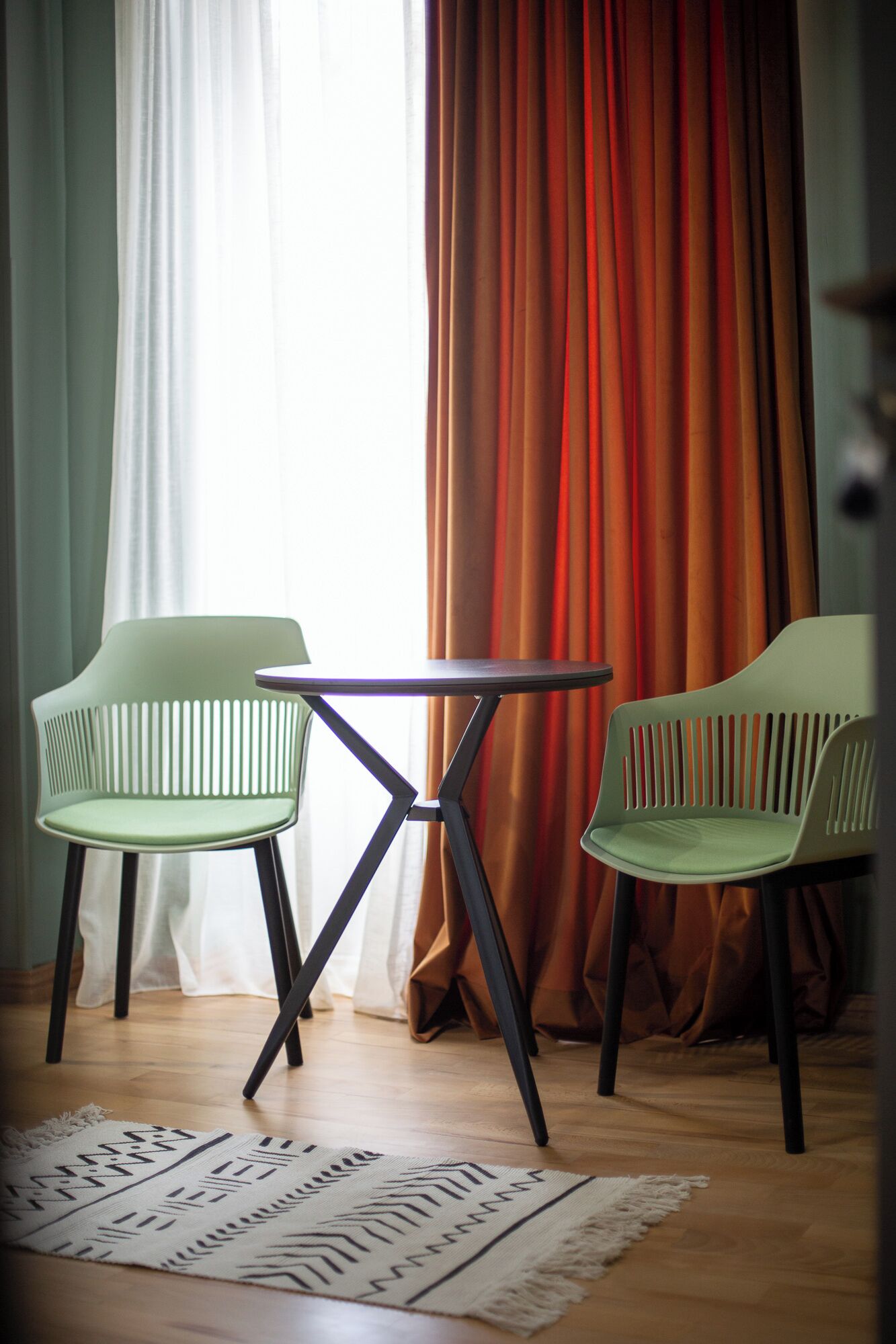 Una habitación con dos sillas, una mesita pequeña, un tapete estampado y cortinas.