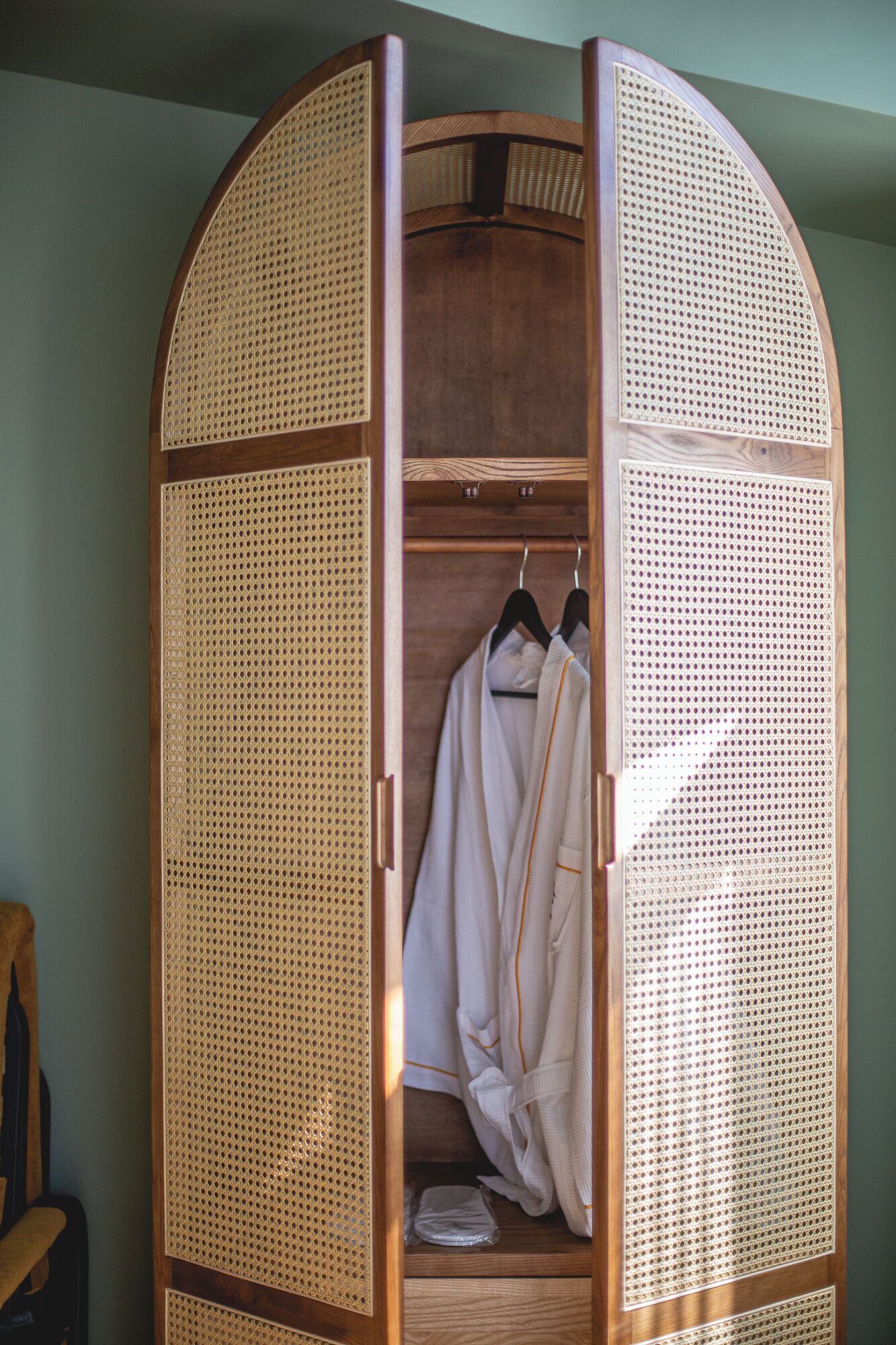 A wooden wardrobe with a semi-open door, featuring a woven back panel and a wooden interior.