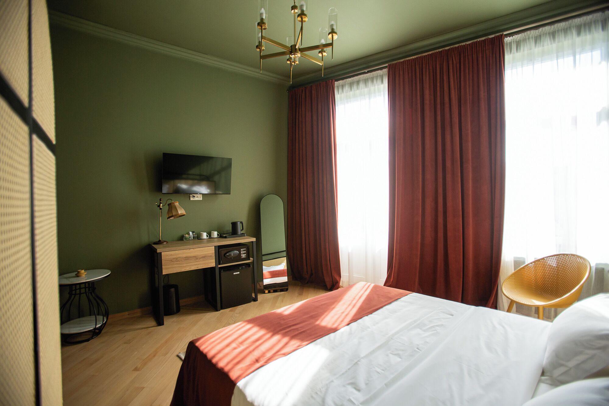 A hotel room with a bed, a desk with a lamp, a television, and a chair.