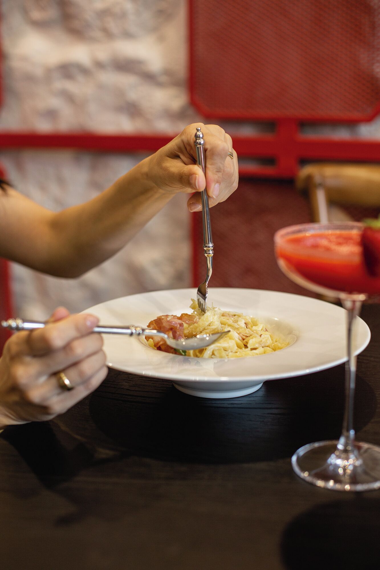 A person dining at a table with a plate of food and a glass of red beverage.