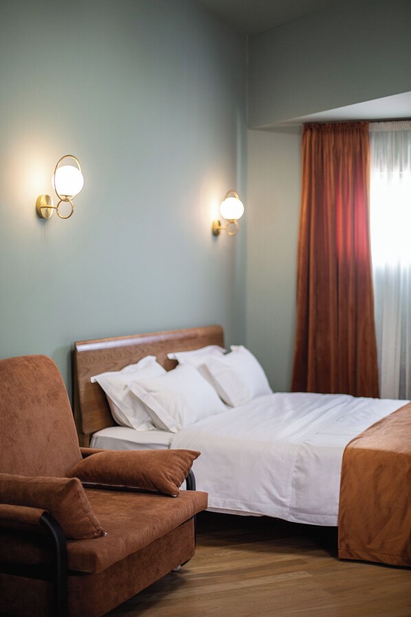 A hotel room with a bed, a brown armchair, and two wall-mounted light fixtures.