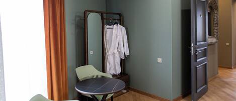 Quarto com piso de madeira, uma cadeira verde, uma mesa pequena, um espelho e um roupão branco pendurado em um suporte.