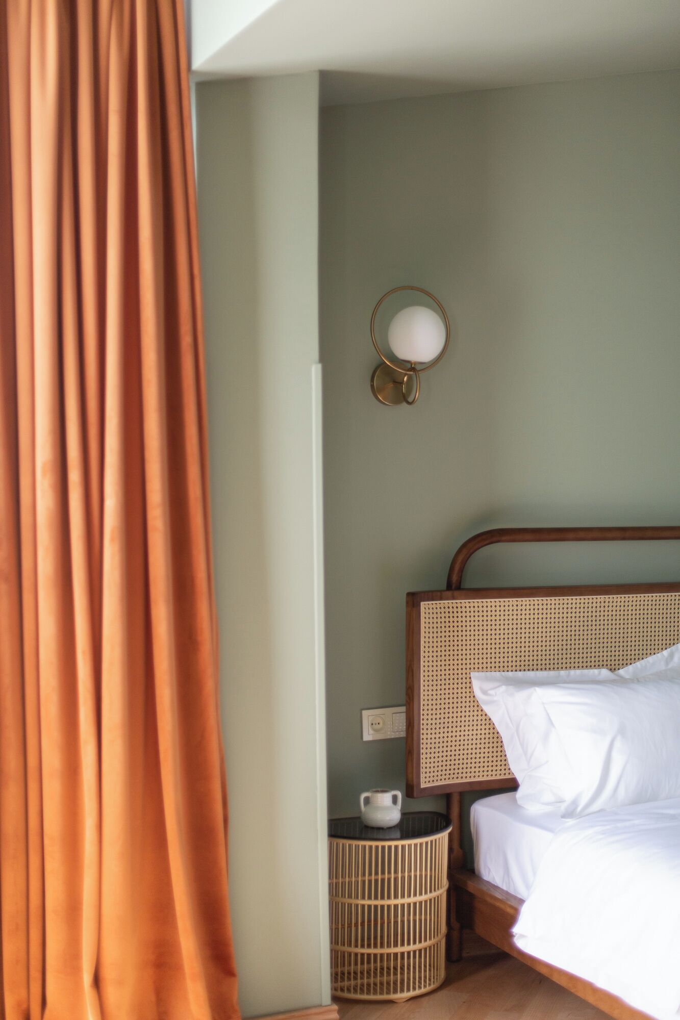 Habitación de hotel con cama, lámpara de pared, una mesita con una taza y una cesta de mimbre.