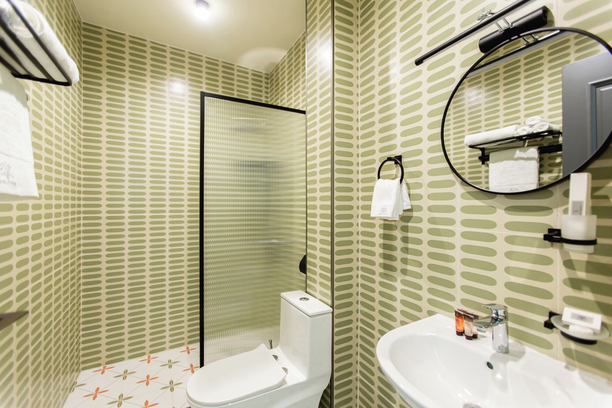 Een badkamer met toilet, wastafel en spiegel. Handdoekrek met handdoeken, zeepdispenser en toiletrolhouder.