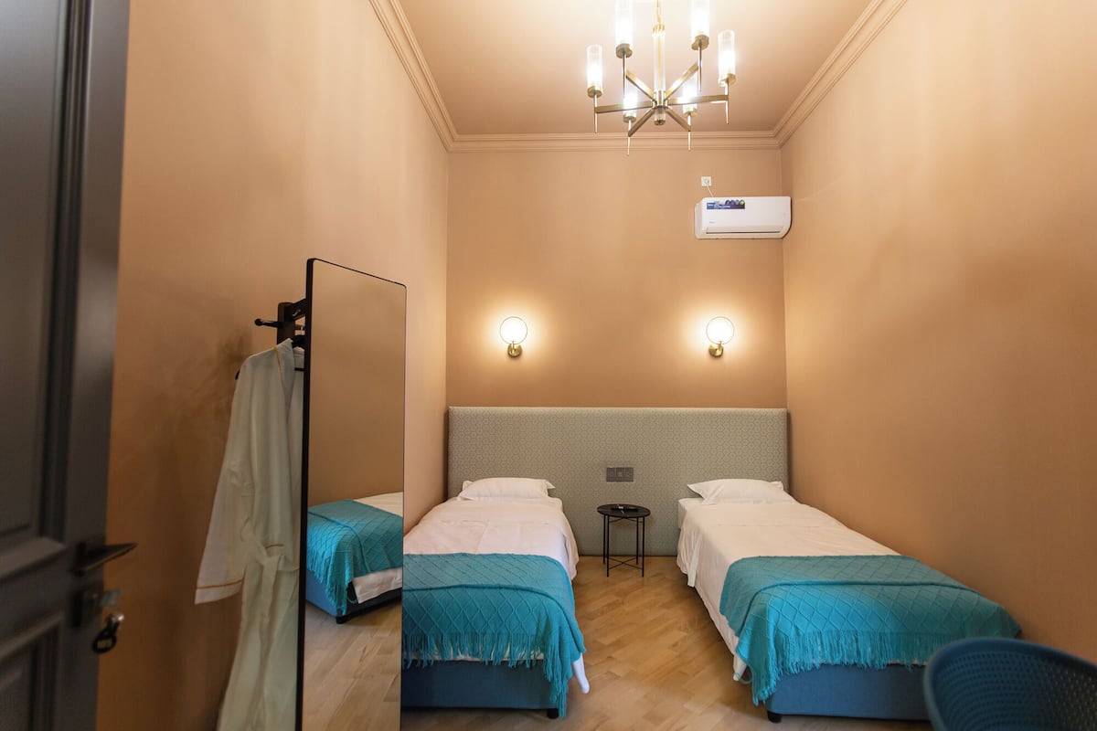 A hotel room with two single beds, a mirror, a ceiling light fixture, and an air conditioning unit.