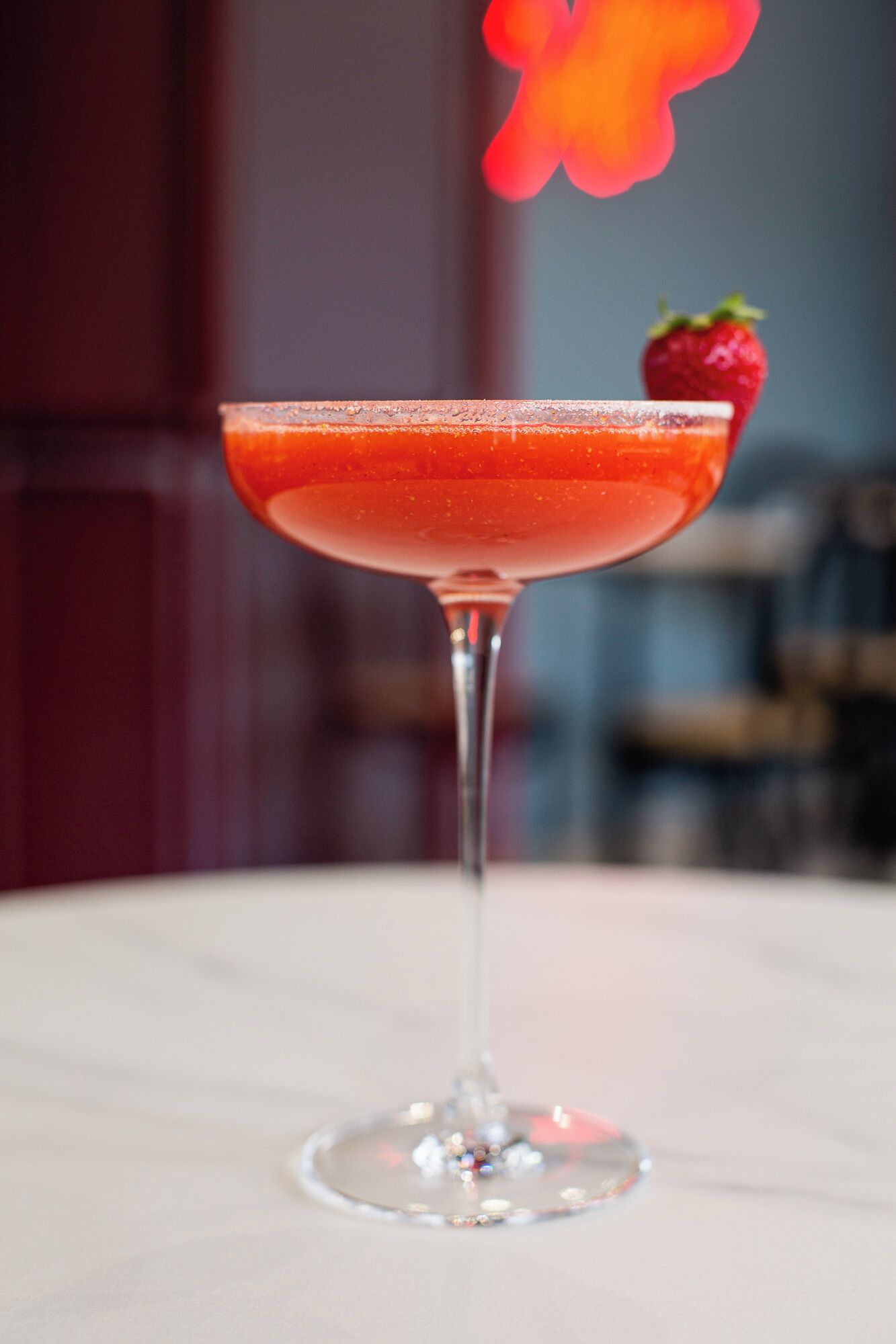 A cocktail glass with a strawberry garnish on a table.