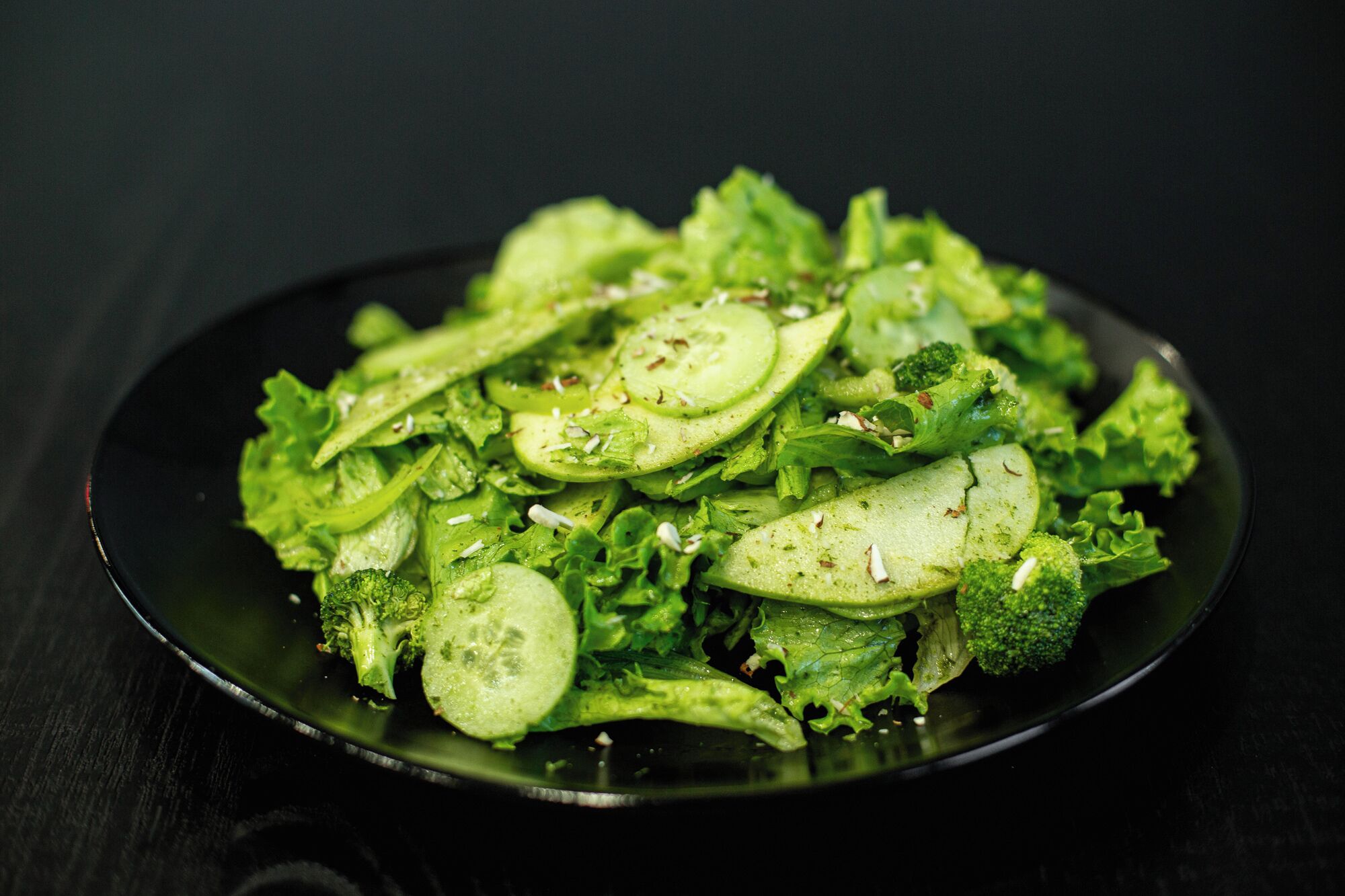 A plate of sliced cucumbers and broccoli on a dark plate.