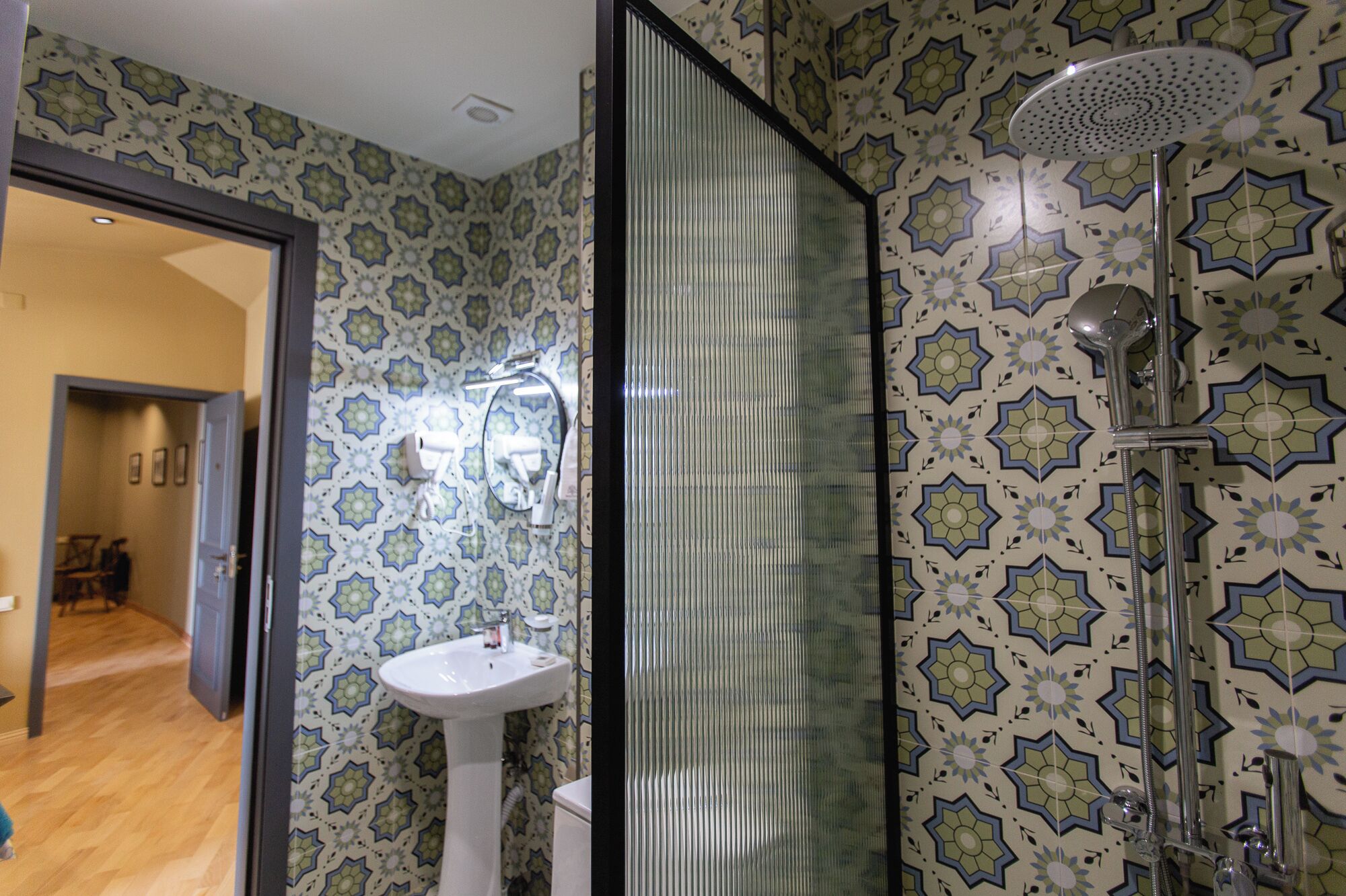 A bathroom with patterned tiles, a white sink, and a shower with a rain showerhead.