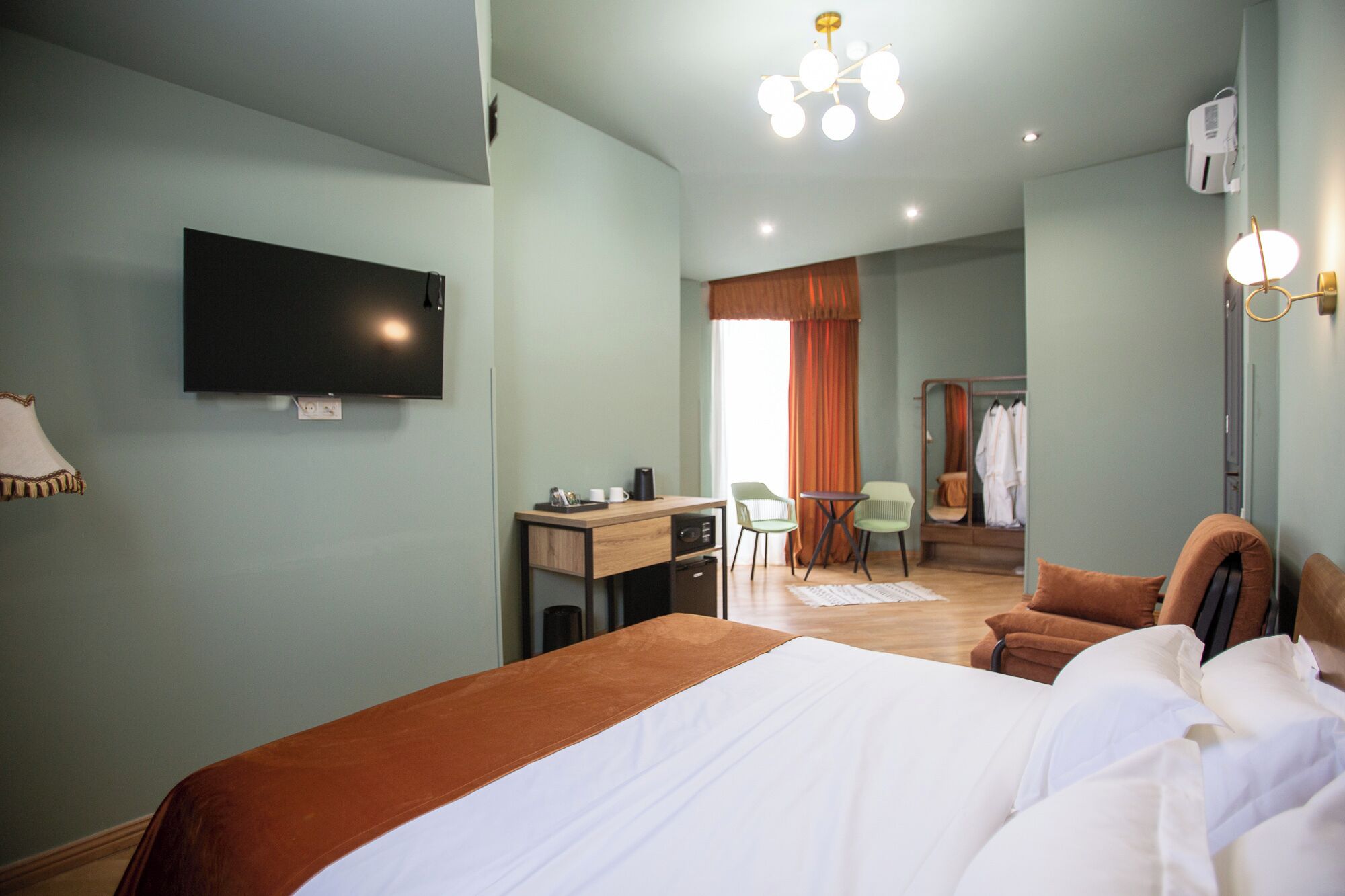 Una habitación de hotel con cama, escritorio, sillas, televisor y armario.