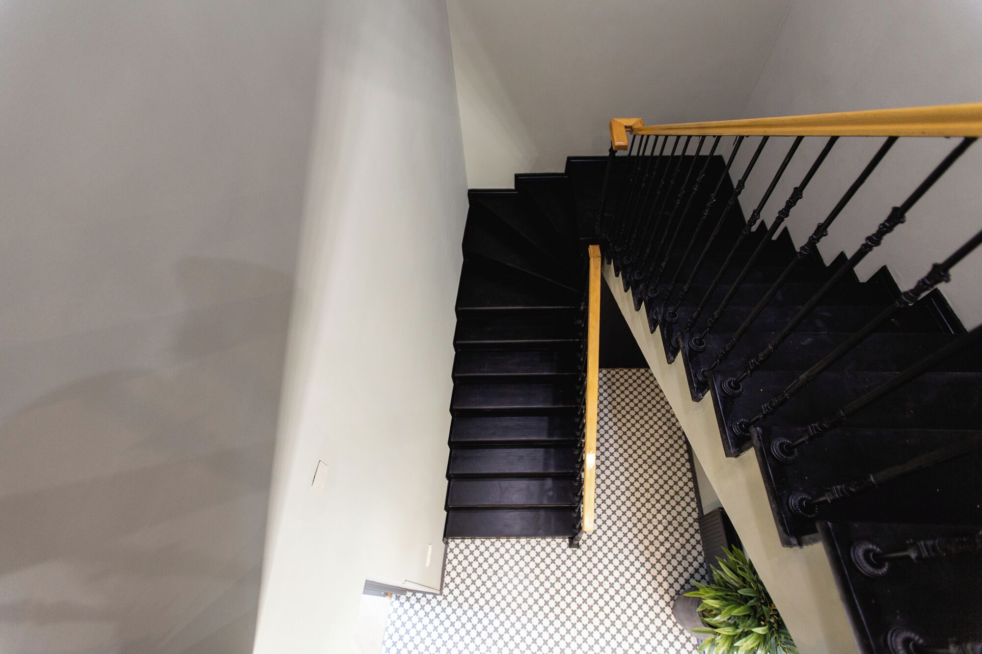 A black staircase with a yellow handrail, leading to a landing with a patterned floor.