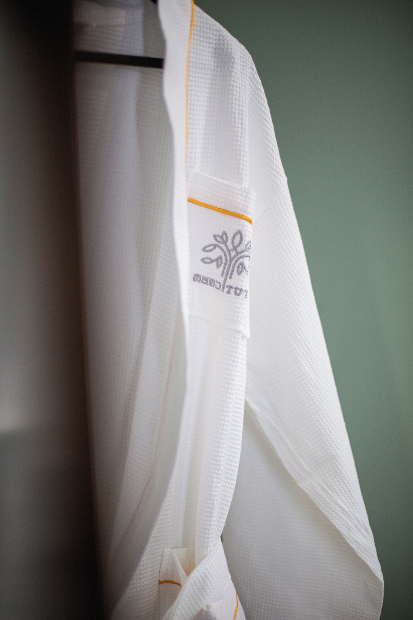 A white garment with a subtle embroidered design and a yellow trim.