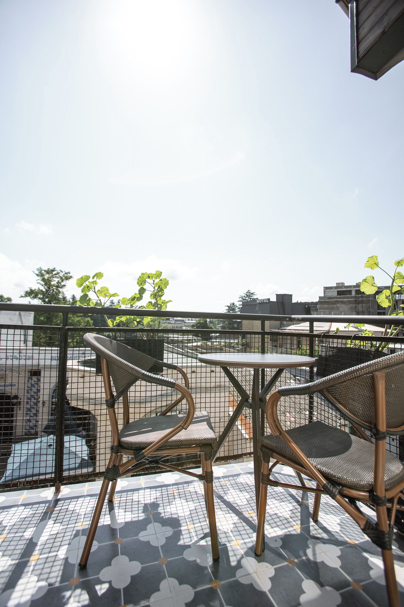 Een terras op het dak met twee rieten stoelen en een kleine ronde tafel, omringd door een metalen hek.