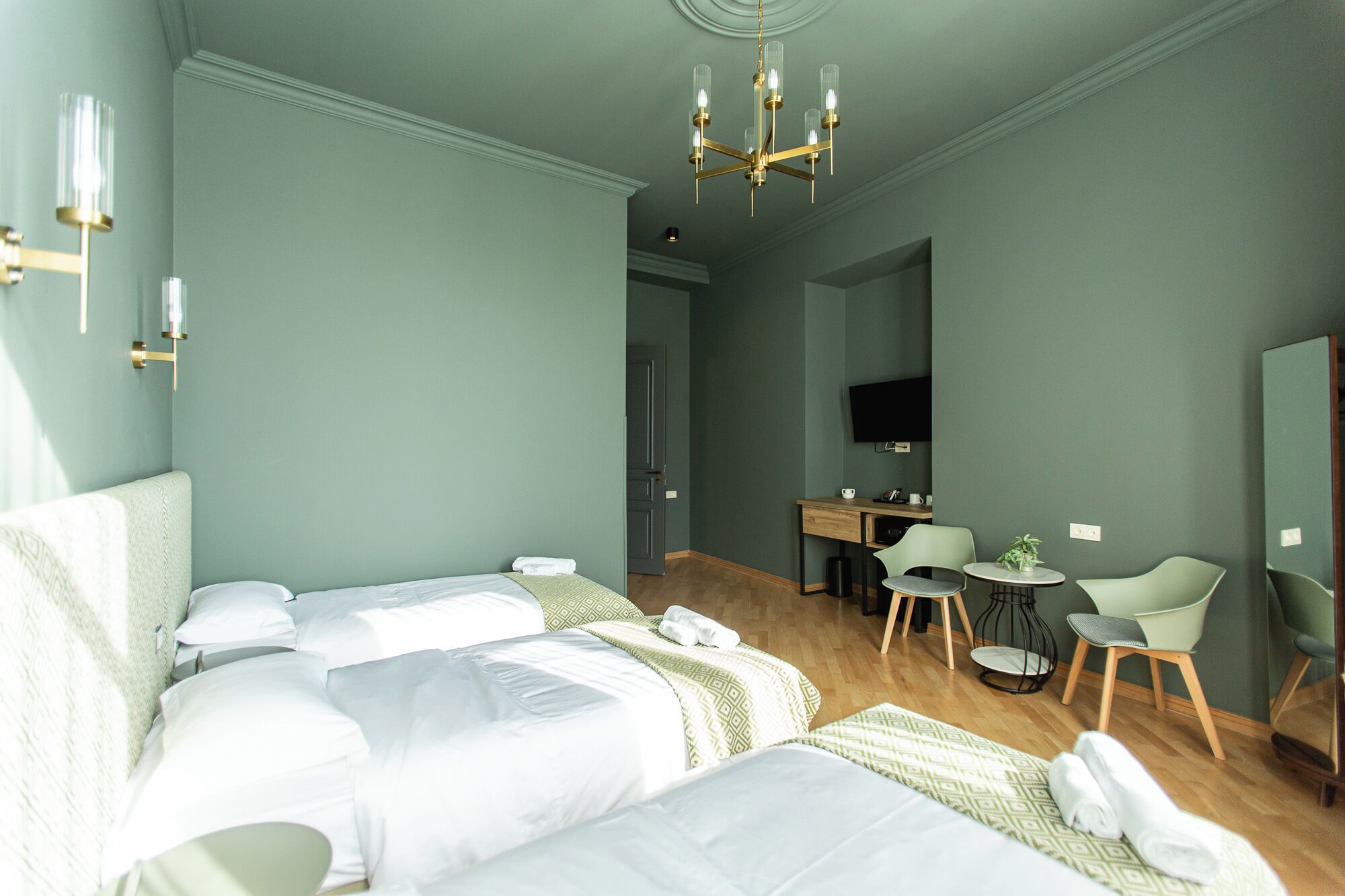 A hotel room with two beds, a desk, a chair, a TV, and a chandelier.