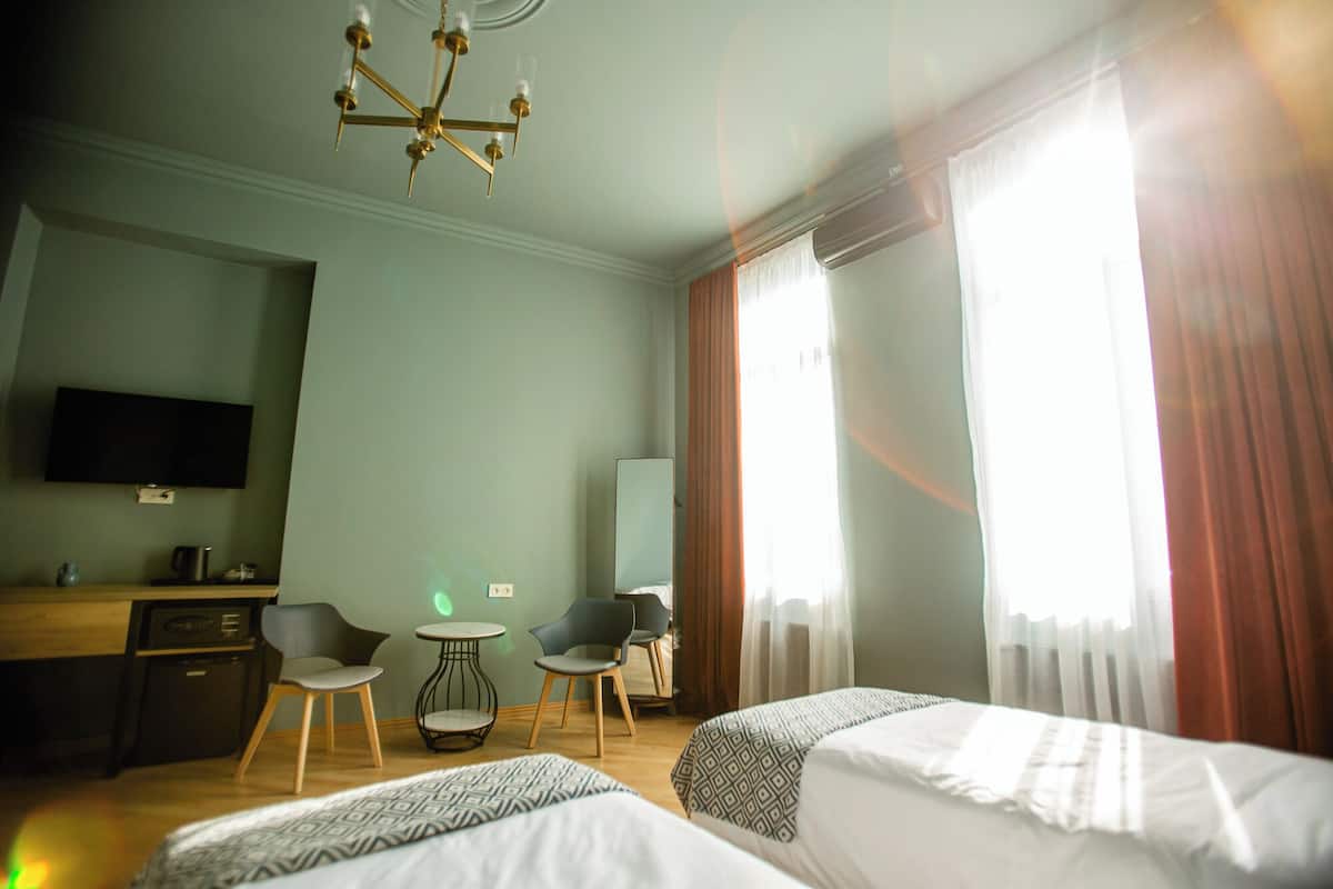 A hotel room with two beds, a desk, a chair, a television, and a chandelier.
