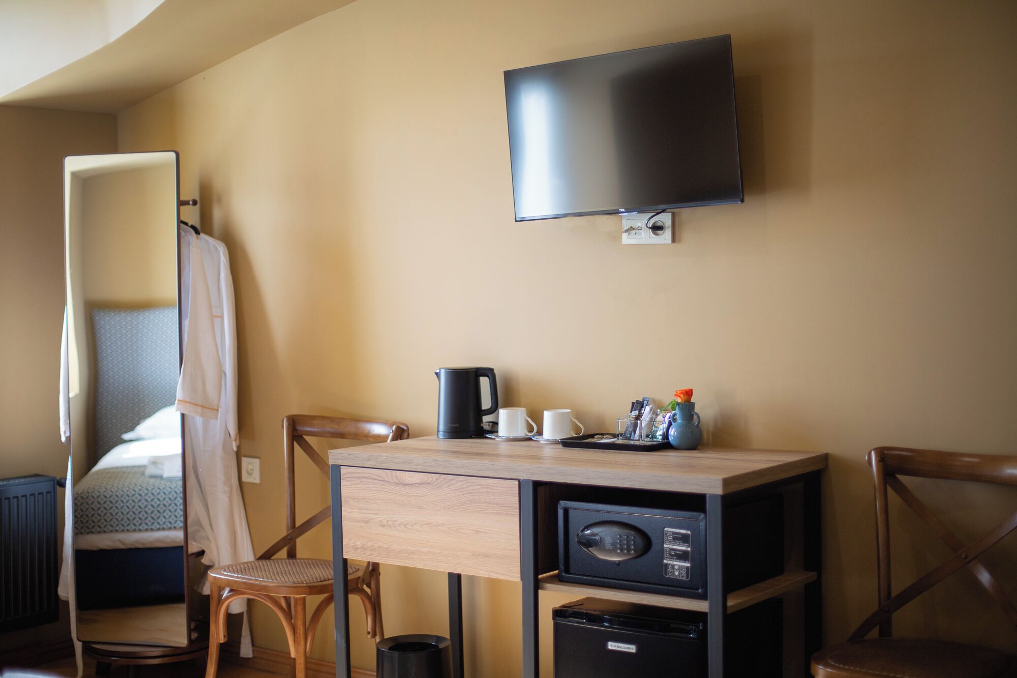 A compact hotel room with a bed, a desk, a chair, a television, and a small refrigerator.