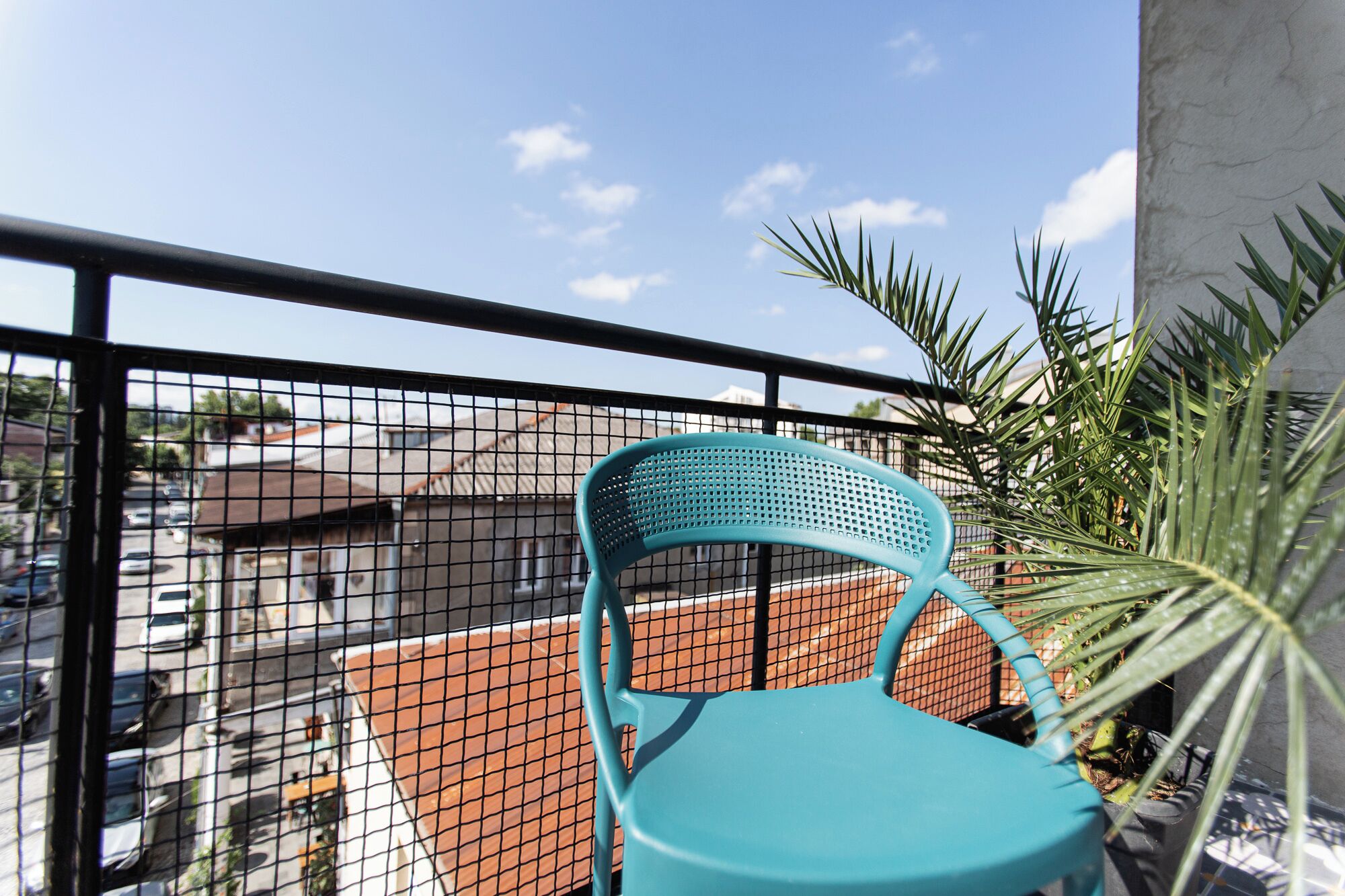 A turquoise chair on a balcony with a view of a parking lot and buildings.