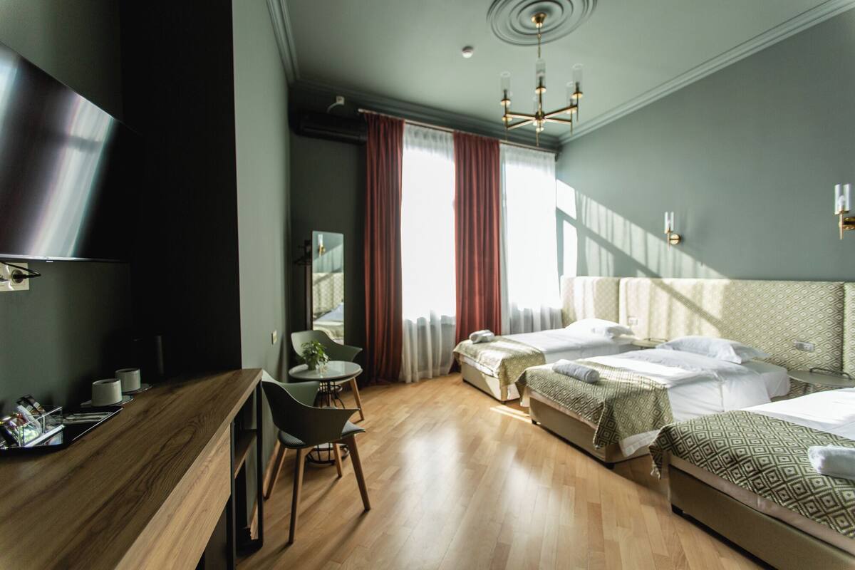 A modern hotel room with a wooden floor, a bed with patterned bedding, a desk with a chair, and a large mirror.
