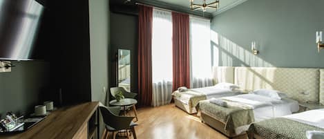 A modern hotel room with a wooden floor, a bed with patterned bedding, a desk with a chair, and a large mirror.