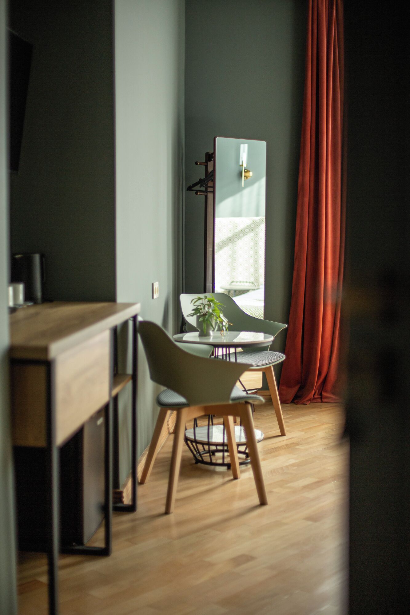 A modern dining area with a wooden table and chairs, a potted plant, and a large mirror reflecting a window view.