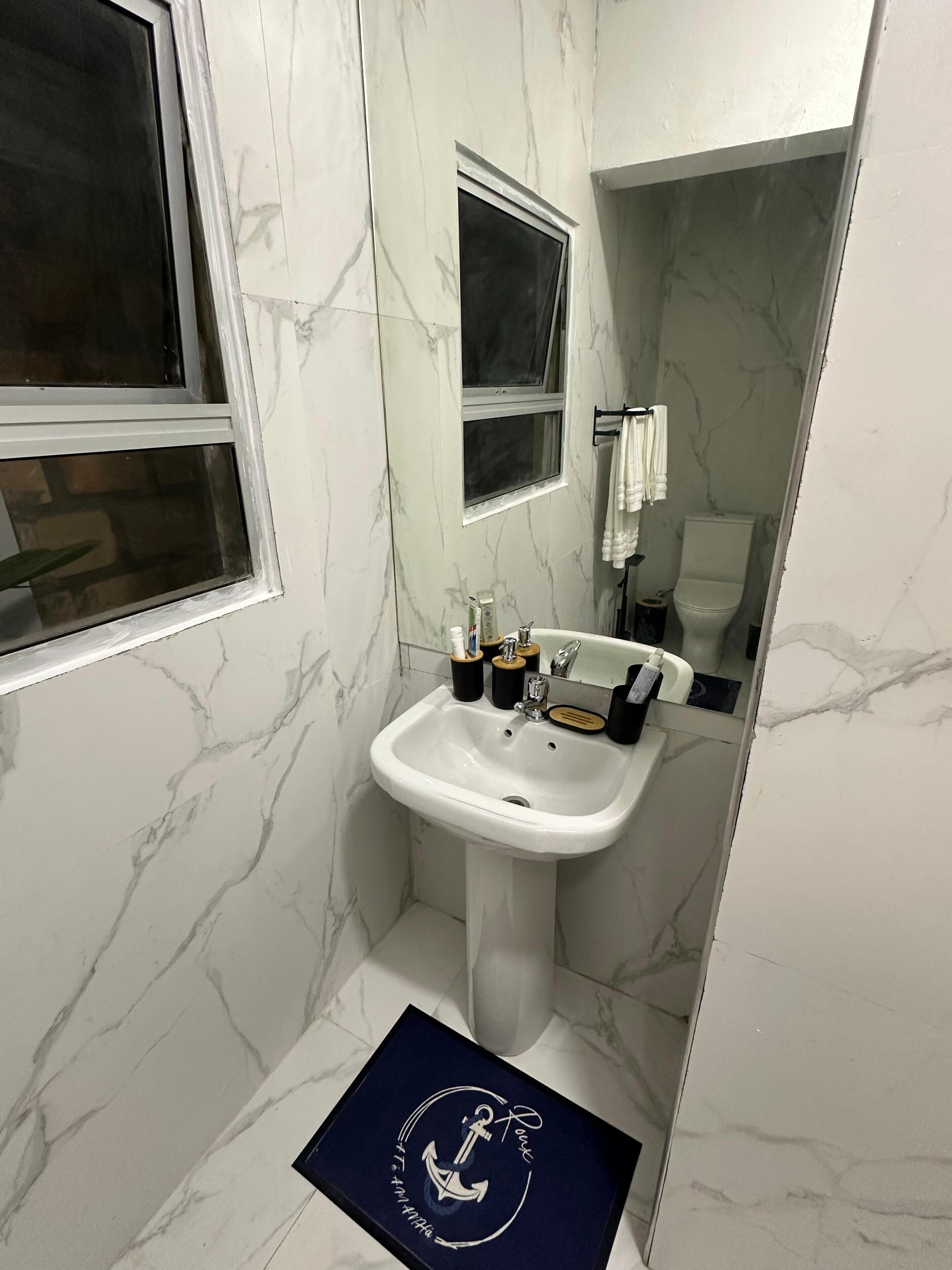 A bathroom with a white marble sink, a window, and a mirror.