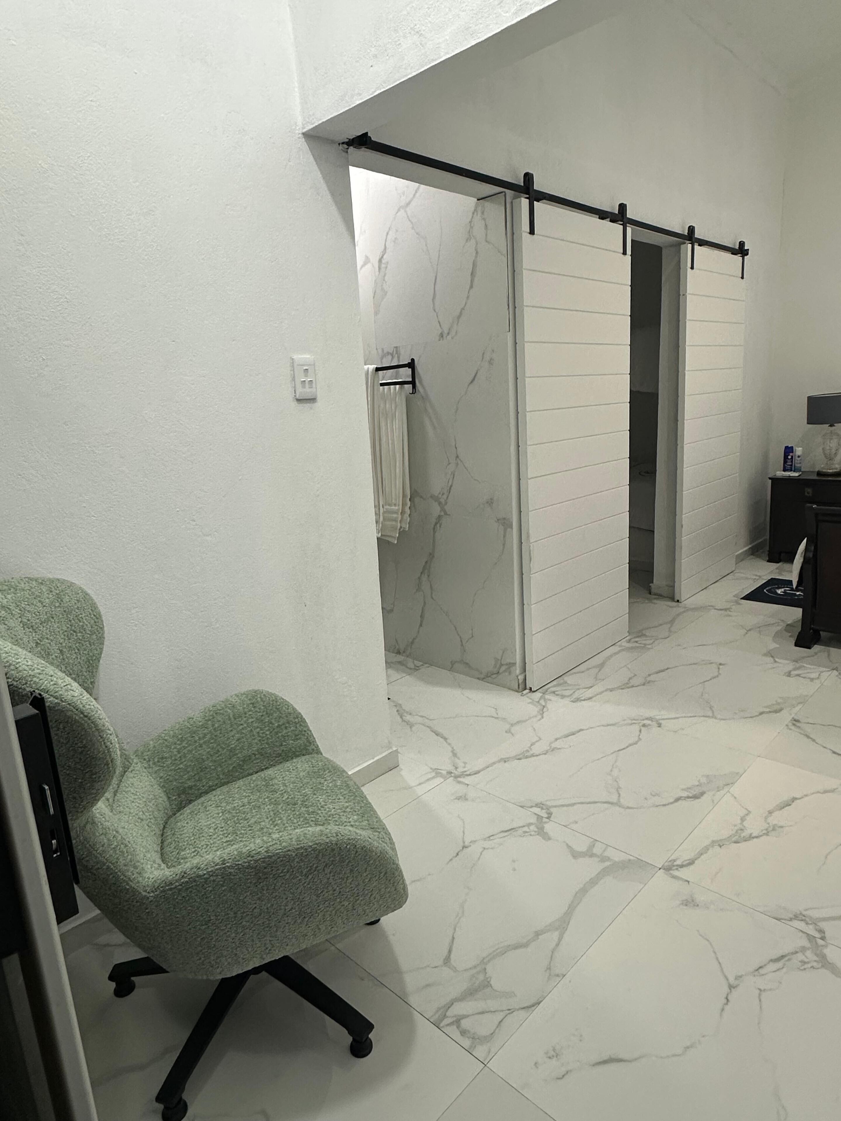 Un baño con ducha, perchero y una silla verde.