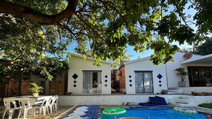 Un espace piscine avec une piscine bleue, deux paniers en osier et un bâtiment blanc doté d’un mur en briques et d’une porte.