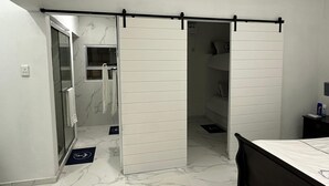 Une chambre à coucher avec un lit, un placard à portes coulissantes, une salle de bain avec une porte en verre et un sol en marbre.