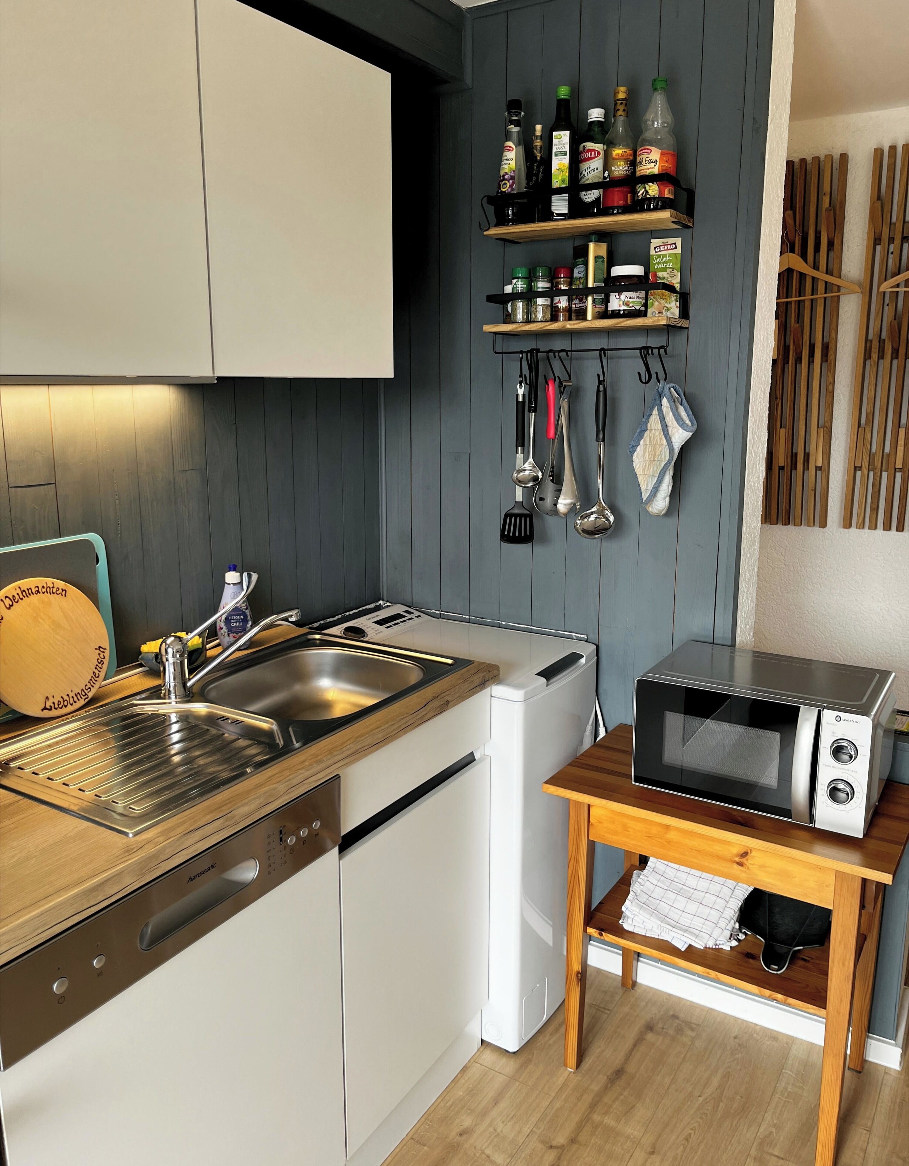A kitchen with a built-in dishwasher, a microwave, a sink with a wooden countertop, and a spice rack.