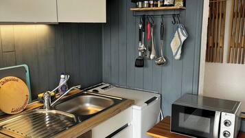 A kitchen with a built-in dishwasher, a microwave, a sink with a wooden countertop, and a spice rack.