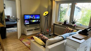 Ein modernes Wohnzimmer mit Flachbildfernseher, einer Couch, einem Essbereich und Blick ins Freie.
