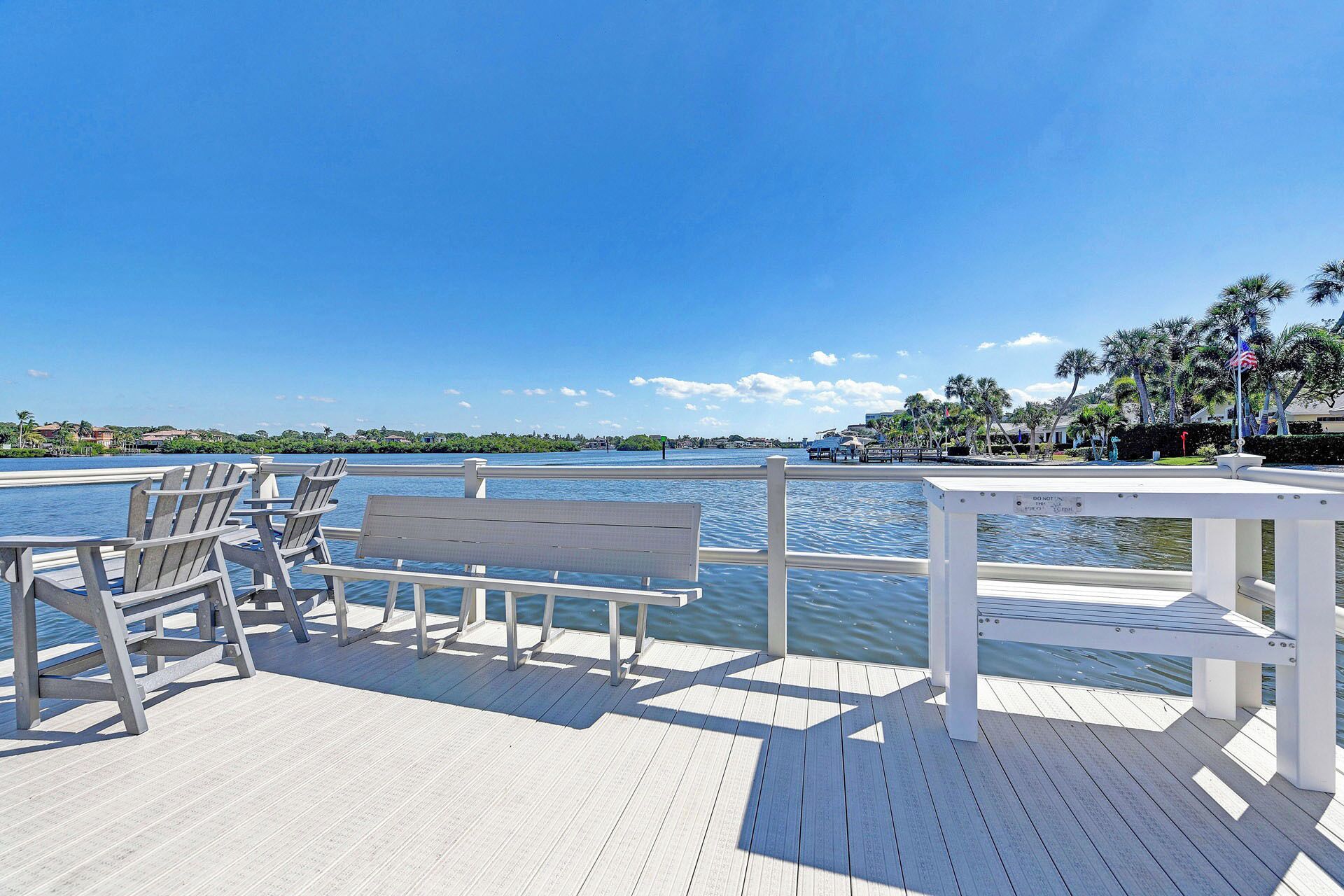 A wooden deck with chairs and a bench overlooking a body of water, with a clear sky above.