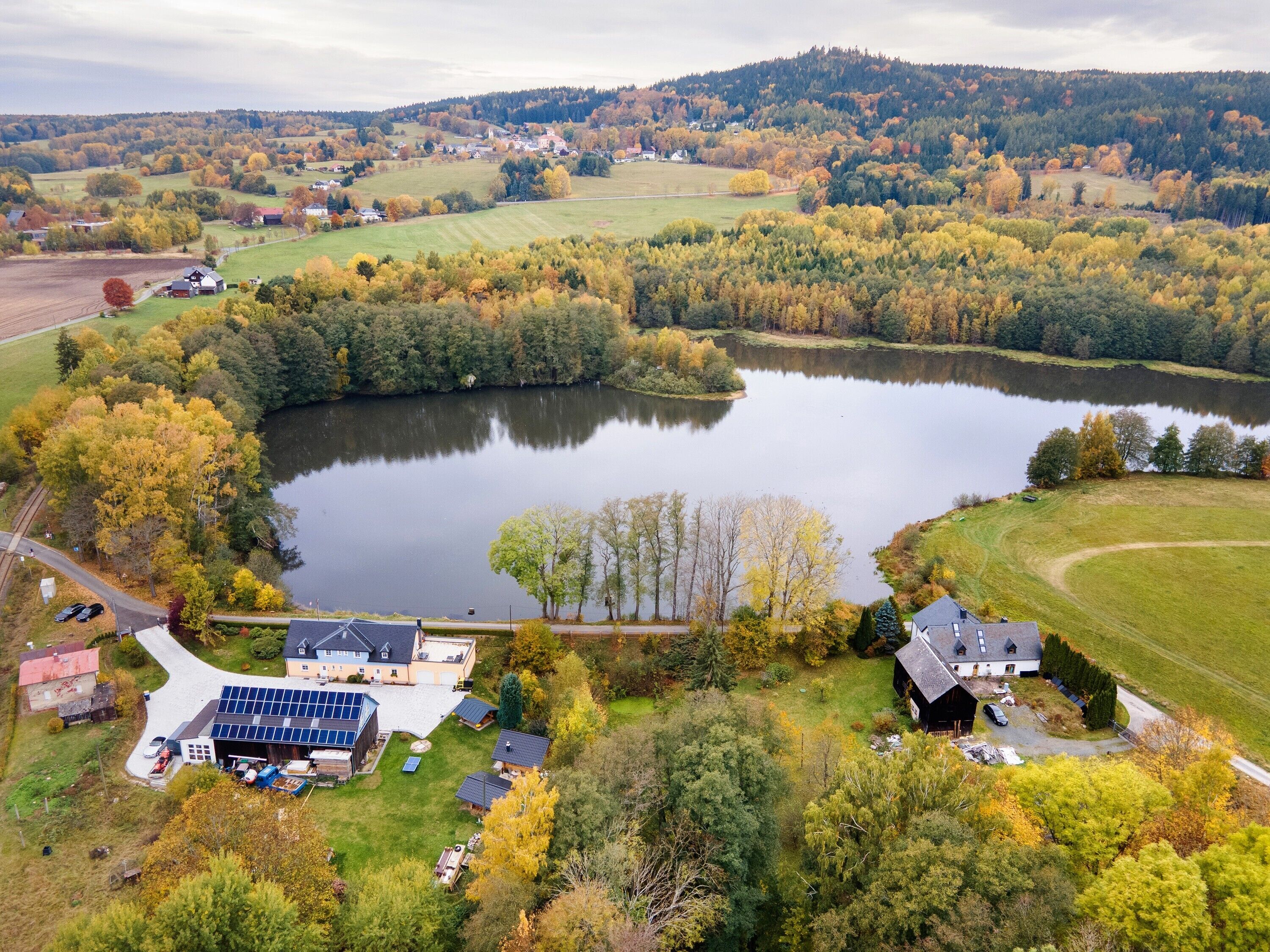 Vue aérienne d’une propriété au bord d’un lac, avec une grande maison, des panneaux solaires et une végétation luxuriante.