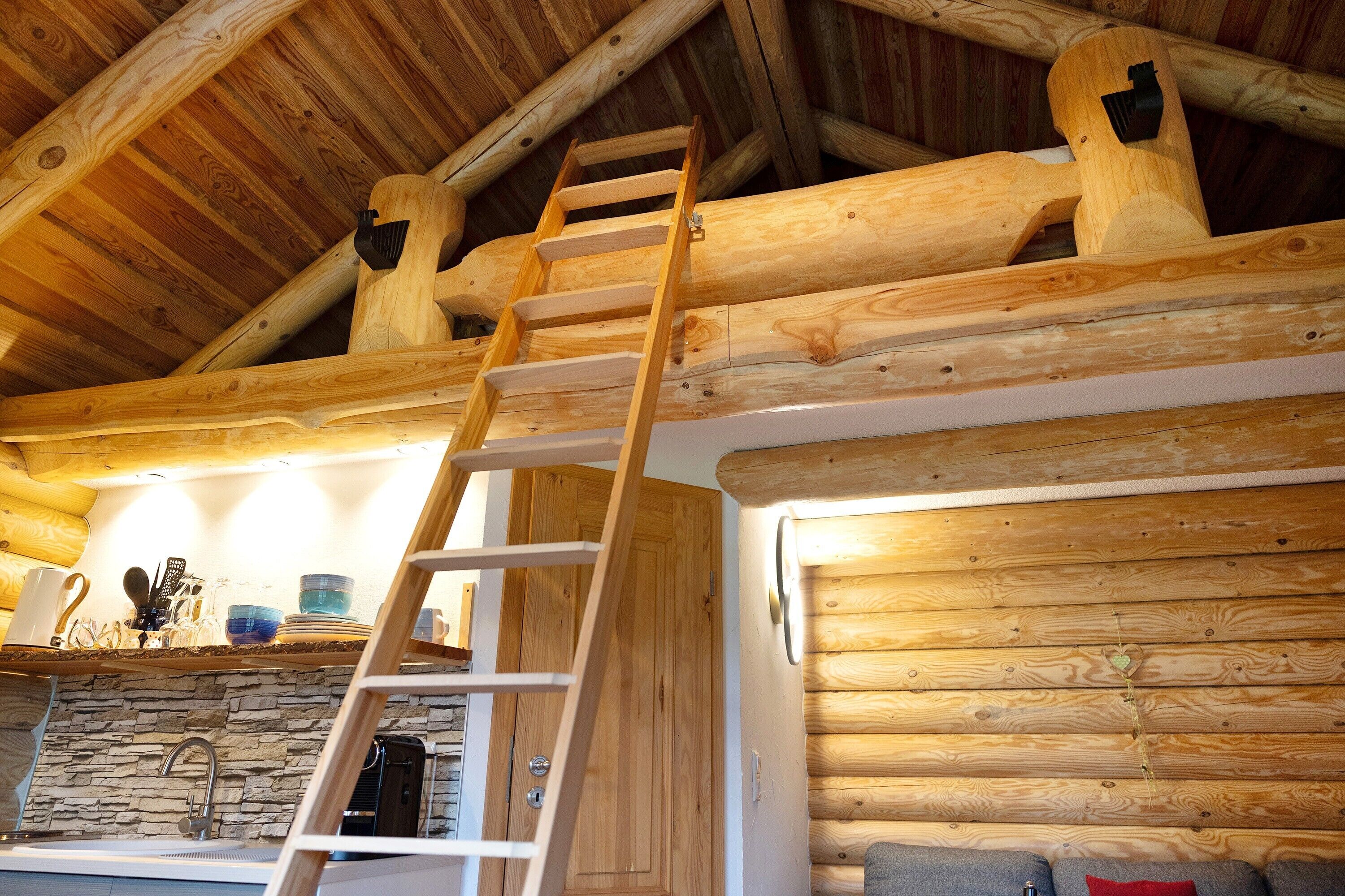 Ein Blockhaus-Interieur mit einer Holzleiter, einer Steinsäule und einem gemütlichen Kamin.