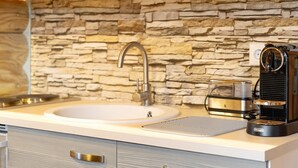 A kitchen with a stone backsplash, a sink, a coffee maker, and a toaster. - Chalet by the Lake – Vogtland Chalet: Cozy Wooden Cabin for Couples (Bad Brambach)