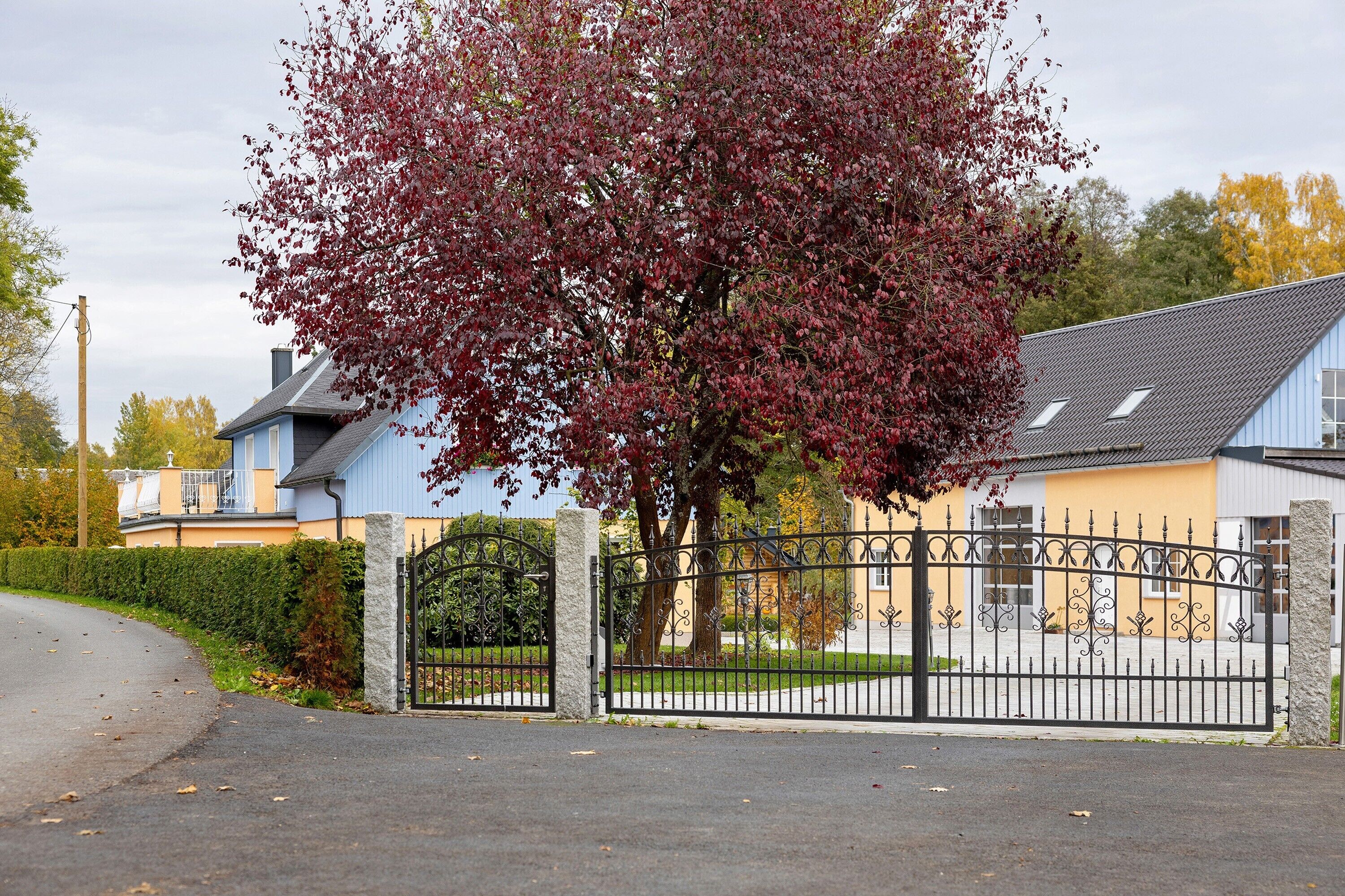 A gated residential area with a house, a tree with red leaves, and a clear sky.