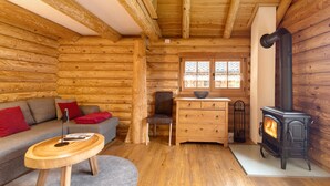 A log cabin interior with a sofa, wooden dresser, and a wood-burning stove. - Chalet by the Lake – Vogtland Chalet: Cozy Wooden Cabin for Couples (Bad Brambach)