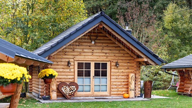 A log cabin with a wooden door, a heart-shaped decoration, and a pumpkin on the porch. - Chalet by the Lake – Vogtland Chalet: Cozy Wooden Cabin for Couples (Bad Brambach)