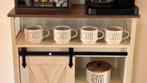A coffee station with a Keurig coffee maker, coffee pods, and mugs on a wooden shelf.