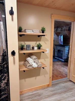 Een houten interieur met een beige muur, een open haard en planken met handdoeken en planten.