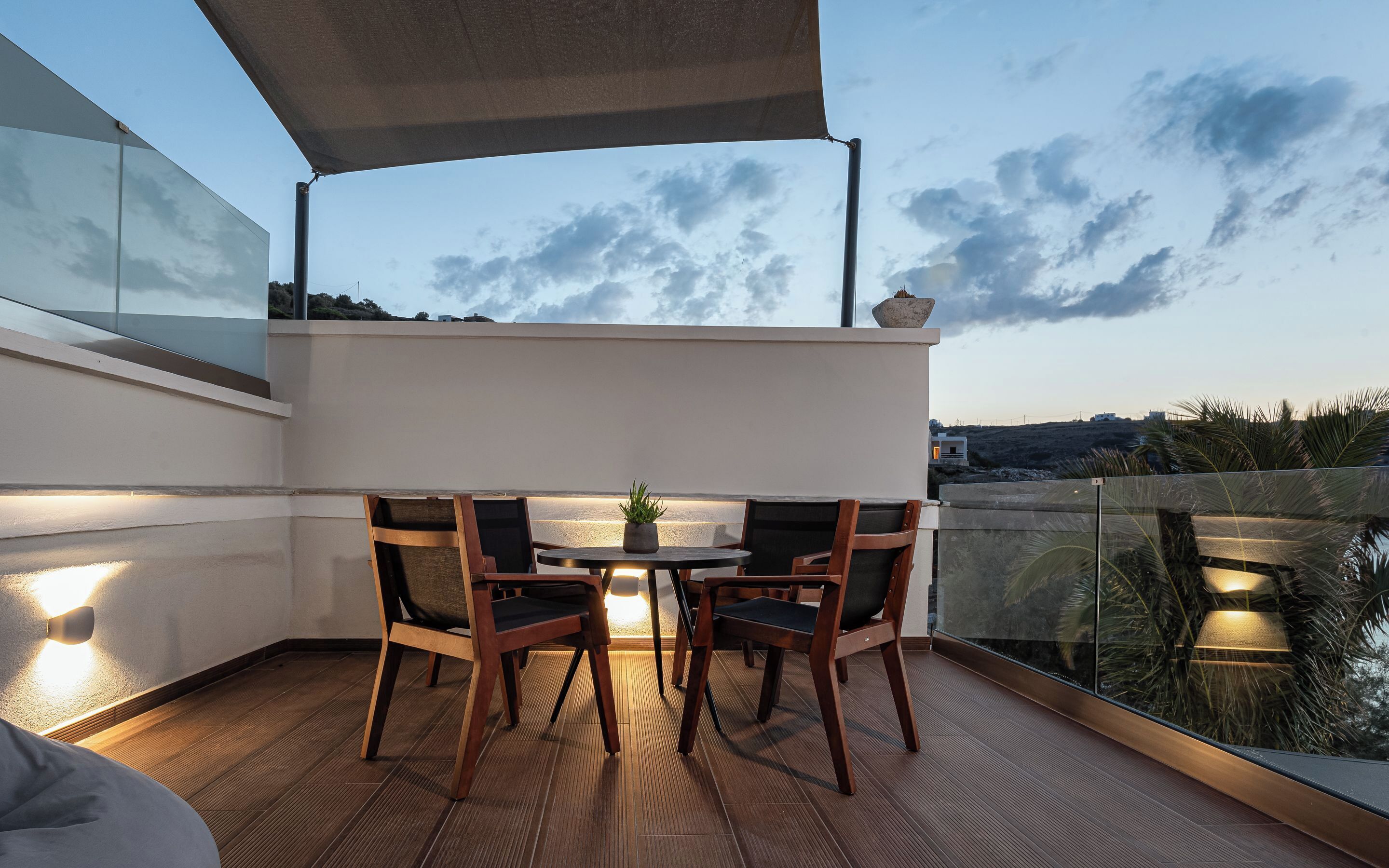 A terrace with a table and chairs, a potted plant, and a view of the landscape.