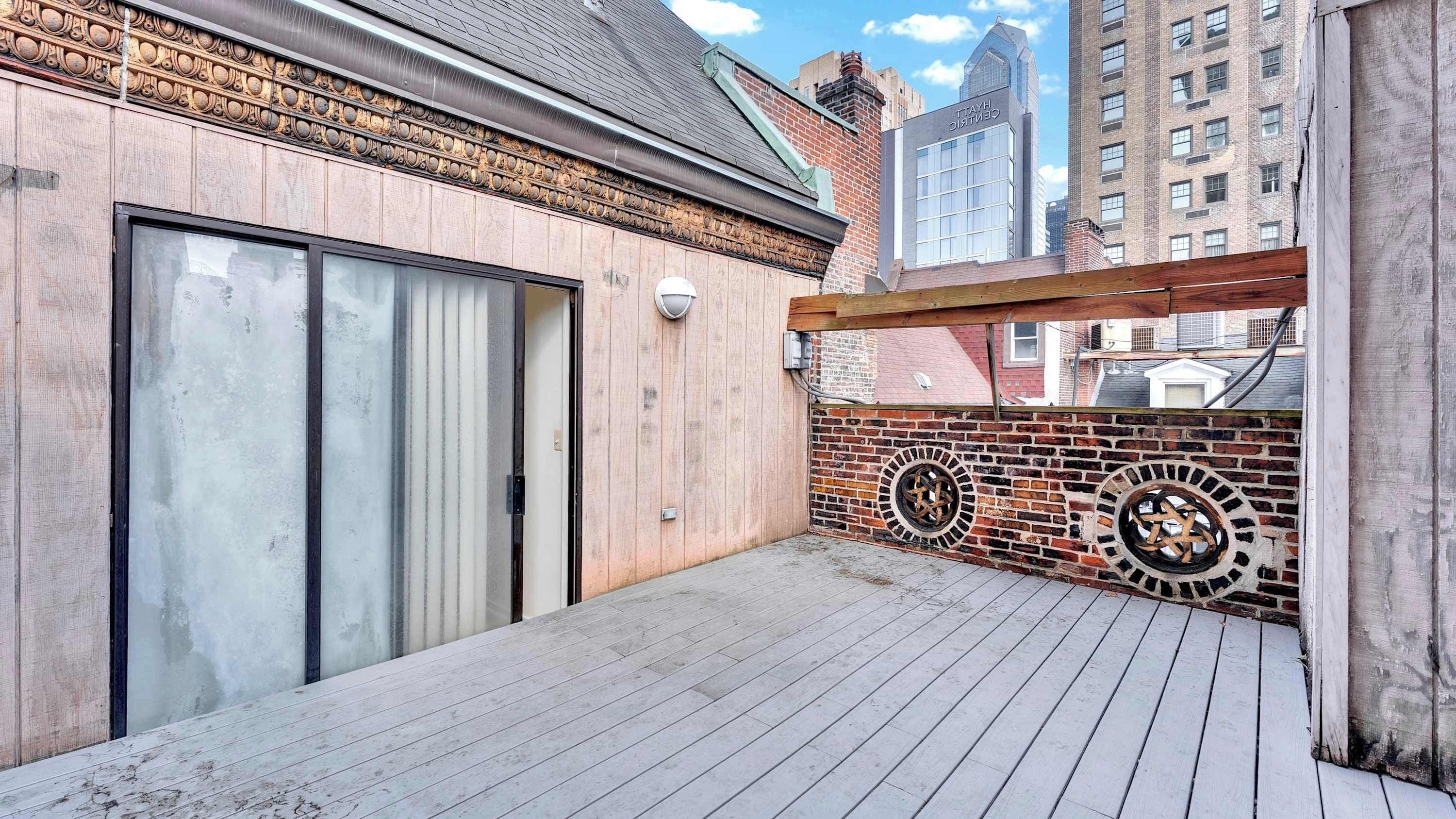 A rooftop patio with a wooden deck, a sliding glass door, and a brick wall with decorative circular windows.