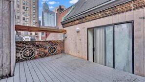 A rooftop patio with a wooden deck, a brick wall with circular windows, and a large sliding glass door.