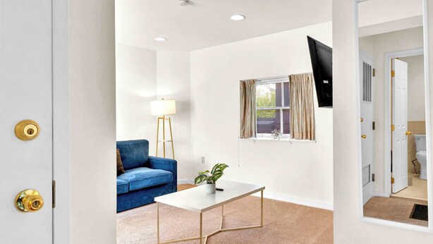 A room with a blue sofa, a white coffee table, a potted plant, a window with curtains, and a flat-screen TV mounted on the wall. - Urban 1BR | Sleeps 4 | Steps to Rittenhouse Square (Philadelphia)