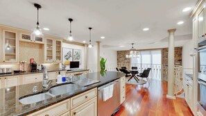 A modern kitchen with granite countertops, stainless steel appliances, and a dining area with a stone wall backdrop. - Grand Queen Village Retreat in Philly | Sleeps 16 (Philadelphia)