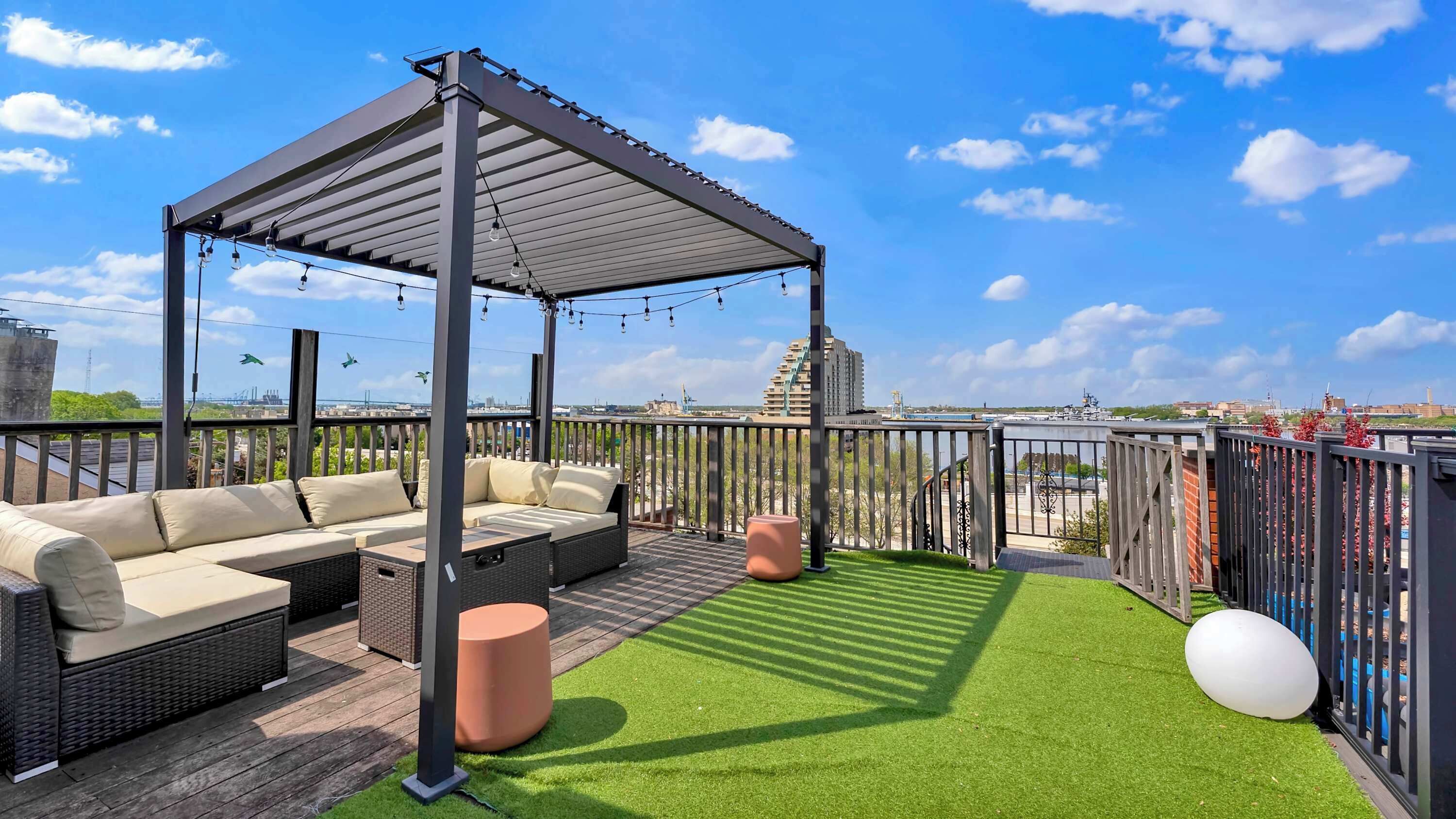 Une terrasse sur le toit dotée d’une pergola, d’un espace salon extérieur, d’un gazon synthétique et offrant une vue sur le paysage urbain.